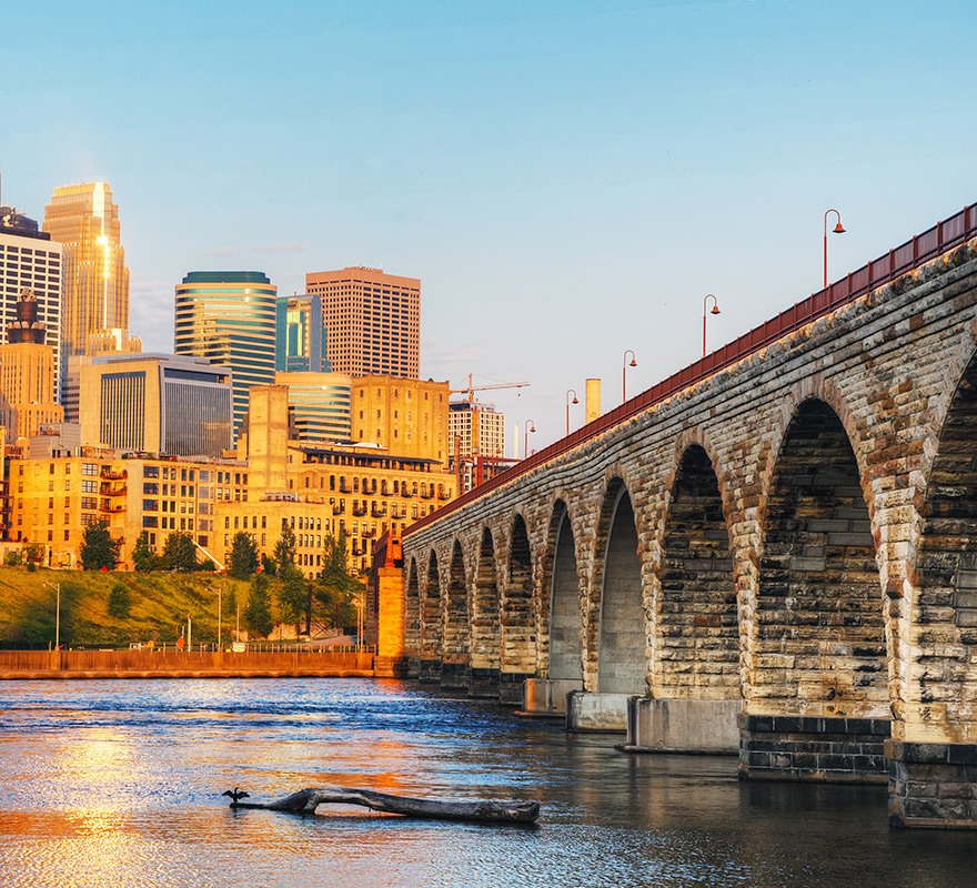 sunset photo of a stone arch bridge on the water with city building in the background